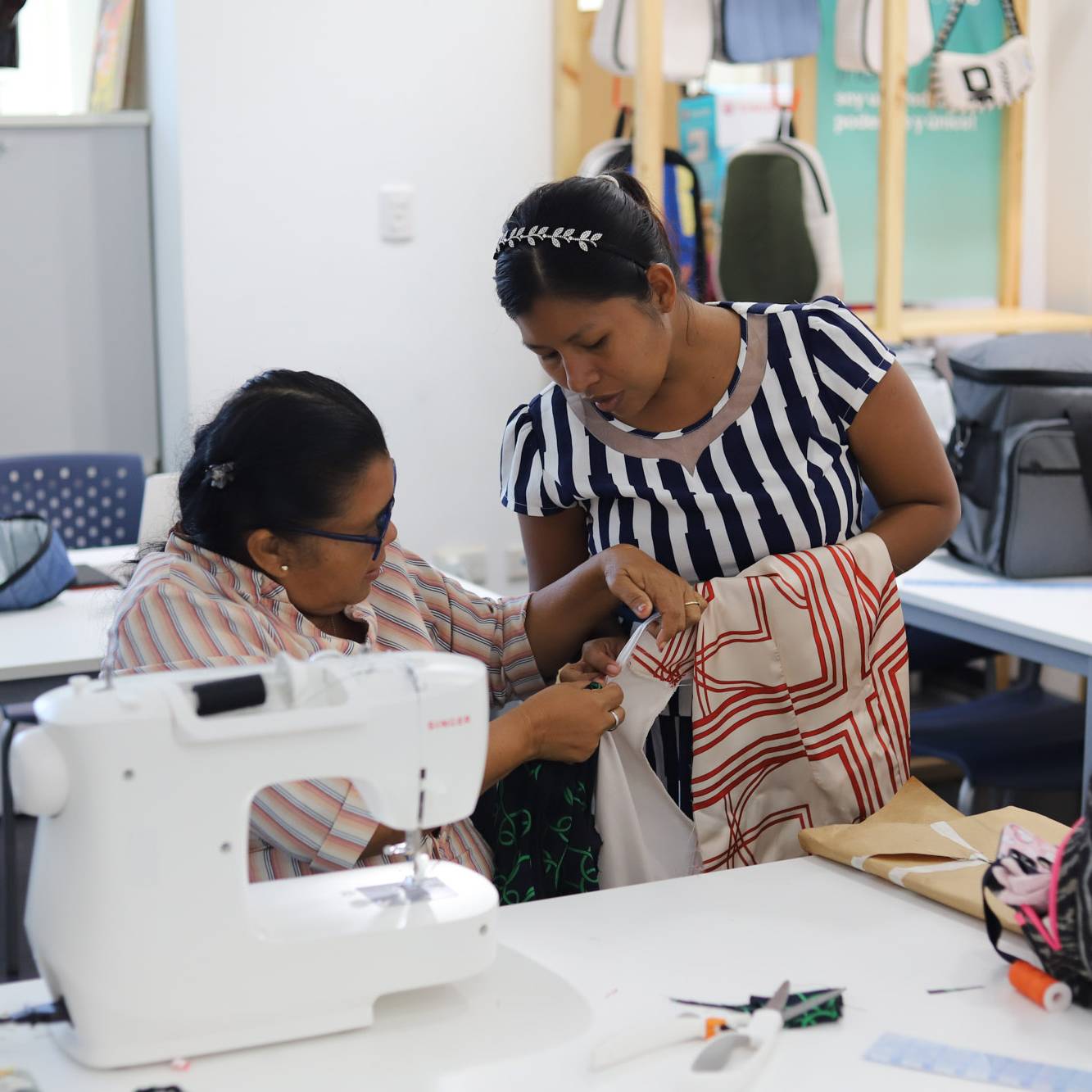 Dos mujeres trabajando juntas en una máquina de coser Singer durante un taller de confección textil en Fundación Estudio TAC.