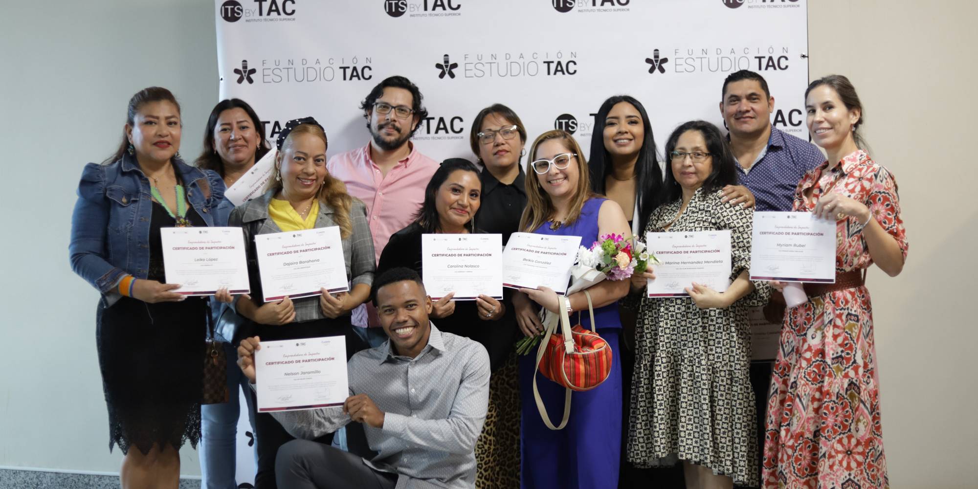 Grupo de graduados posando con sus certificados de participación frente al fondo de prensa de Fundación Estudio TAC e ITS by TAC.