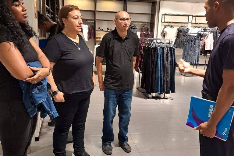 Un instructor con libreta en mano brinda orientación sobre dinámicas de retail y atención al cliente a participantes del programa Yo Aprendo dentro de una tienda de indumentaria.