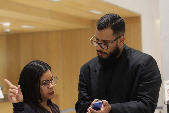 Un facilitador y una participante del programa Yo Aprendo revisan herramientas digitales junto a un perchero de indumentaria durante una práctica comercial.
