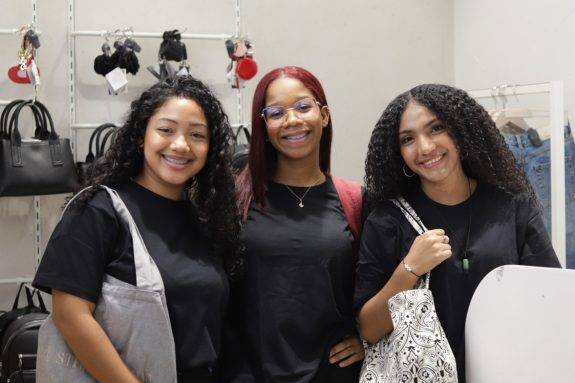 Tres jóvenes participantes del programa Yo Aprendo sonríen juntas llevando bolsos de tela durante una actividad práctica de formación en una tienda comercial.