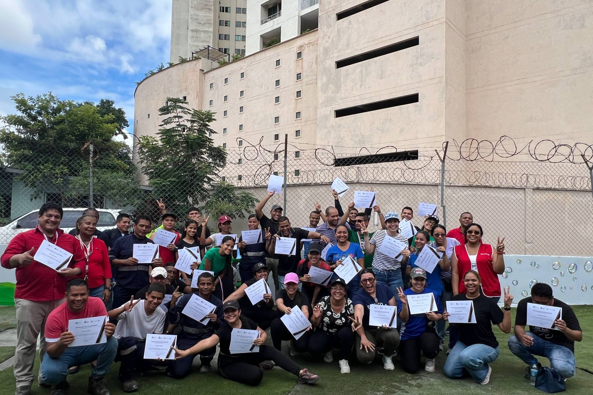 Participantes, voluntarios y coordinadores del programa Yo Aprendo participan alegremente en una jornada comunitaria y de voluntariado al aire libre, colaborando en equipo en la pintura de murales, la creación de mobiliario reciclado y la celebración de sus logros.