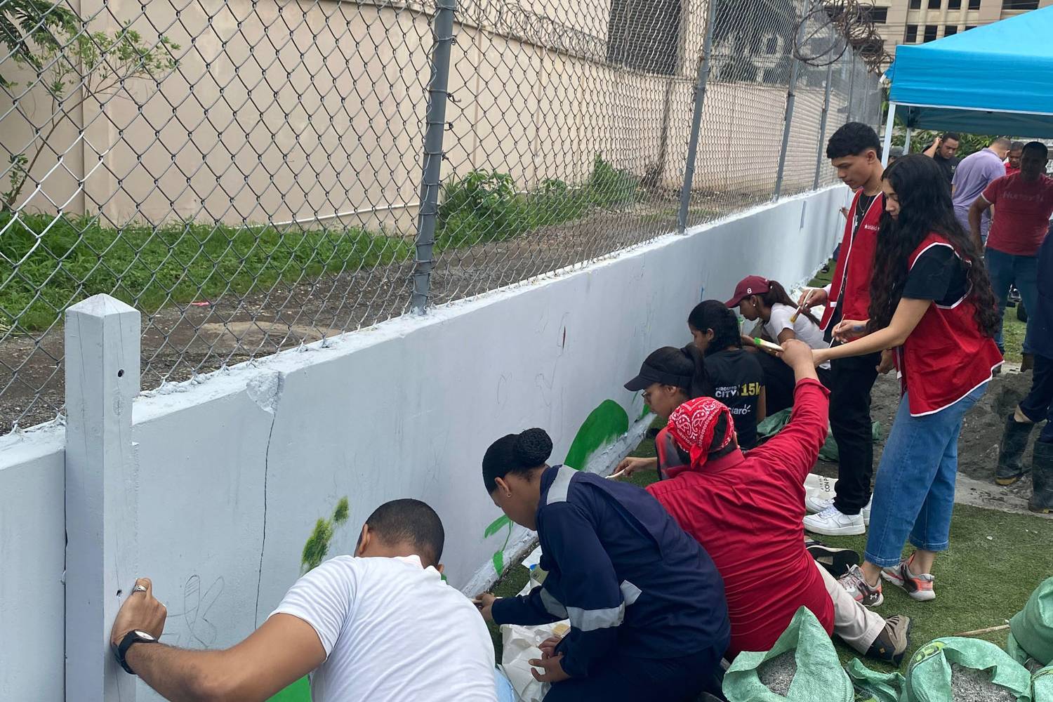 Participantes, voluntarios y coordinadores del programa Yo Aprendo participan alegremente en una jornada comunitaria y de voluntariado al aire libre, colaborando en equipo en la pintura de murales, la creación de mobiliario reciclado y la celebración de sus logros.