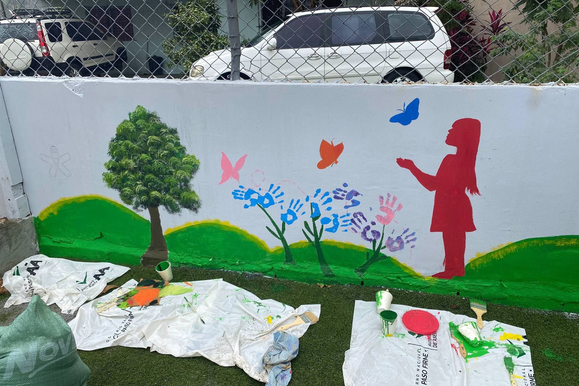 Participantes, voluntarios y coordinadores del programa Yo Aprendo participan alegremente en una jornada comunitaria y de voluntariado al aire libre, colaborando en equipo en la pintura de murales, la creación de mobiliario reciclado y la celebración de sus logros.