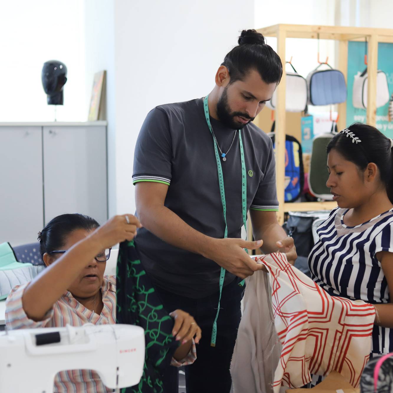Un instructor con cinta m&eacute;trica asesora a dos participantes en la selecci&oacute;n y corte de telas estampadas dentro del taller de costura del programa Yo Aprendo.