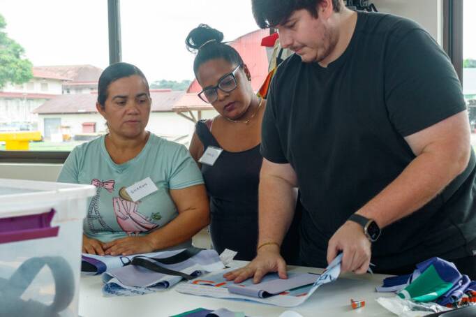 Un instructor de la Fundación Estudio TAC explica técnicas de diseño y confección textil a dos participantes sobre la mesa de trabajo.